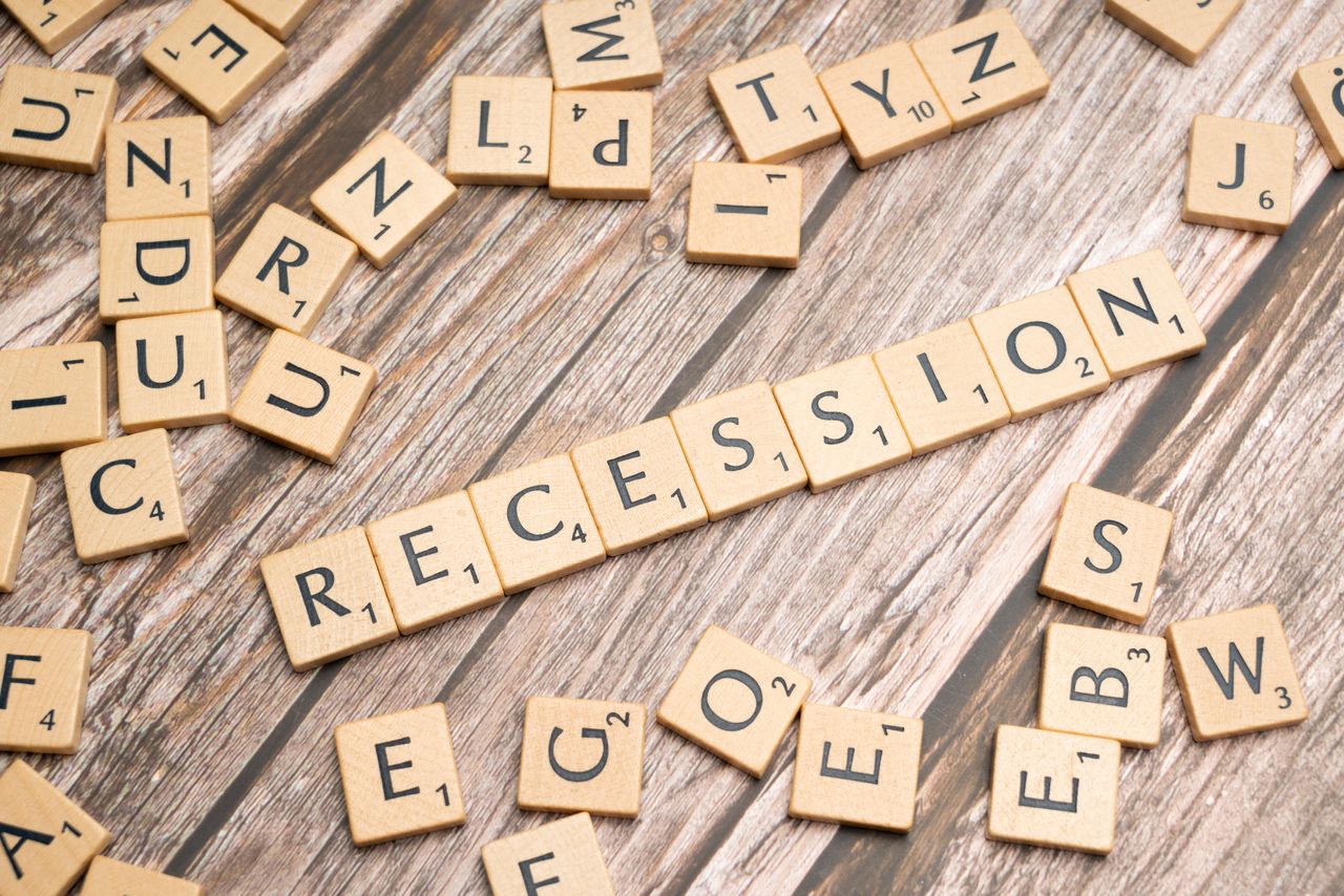 Wooden letter tiles on a wooden surface spell out the word "Recession," symbolizing economic downturn.